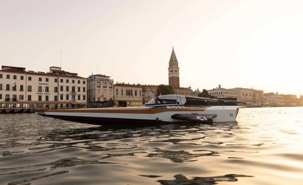La lancha eléctrica RaceBird de la E1 Series flota en las tranquilas aguas de Venecia al amanecer, con la icónica torre del Campanile en la distancia, simbolizando un nuevo despertar para los deportes náuticos sostenibles.